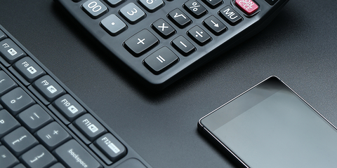 Taschenrechner, Tastatur und ein Smartphone auf einer schwarzen Fläche.