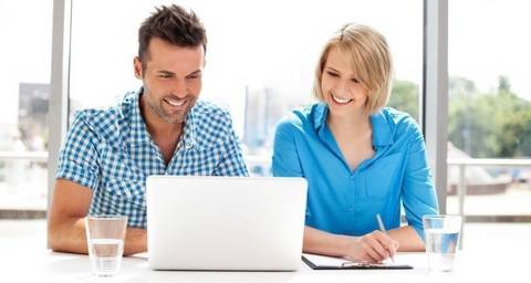 Mann und Frau im Hemd schauen sich lächelnd etwas am Laptop an