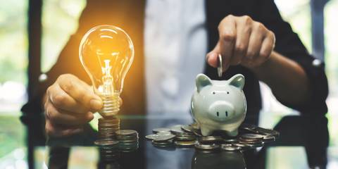 Businessfrau hält eine leuchtende Glühlampe und lässt Münzen in ein Sparschwein fallen