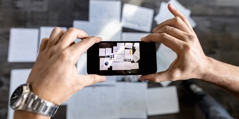 Zwei Hände halten ein Smartphone in der Hand und fotografieren Dokumente 