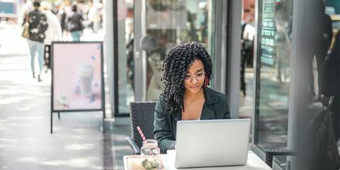 Frau sitzt an einem Straßencafé und arbeitet an einem Laptop