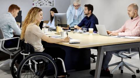 Eine Frau im Rollstuhl sitzt mit Mitarbeitenden am Konferenztisch