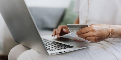 Frau sitzt vor Laptop mit Kreditkarte in der Hand