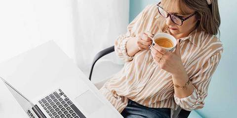 Eine Frau sitzt vor einem Laptop und trinkt einen Kaffee