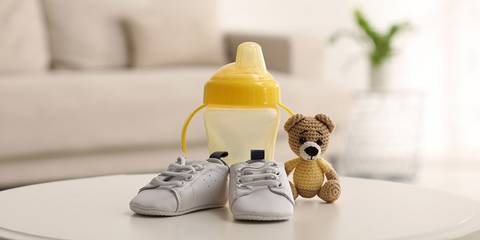 Kinderschuhe, Trinkflasche und kleiner Teddybär auf einem Couchtisch
