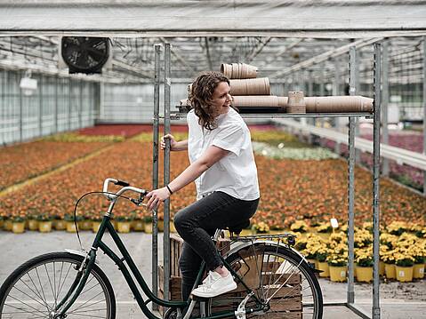 Bild von Lexware: Frau sitzt auf Fahrrad vor einem offenen Gewächshaus mit Blumen