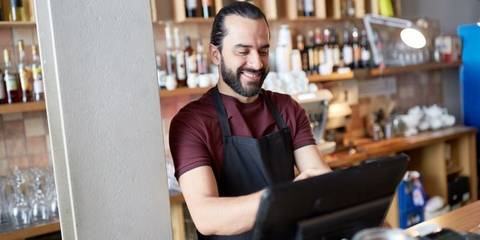 Ein Mann in einer Schürze steht lächelnd hinter einer Bar