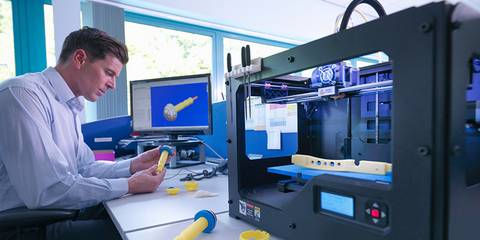 Ein Mann arbeitet an einem Schreibtisch mit einem 3D-Drucker