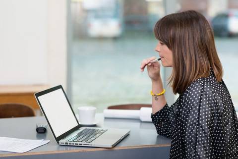 Frau mit Kugelschreiber in der Hand sitzt vor einem Laptop