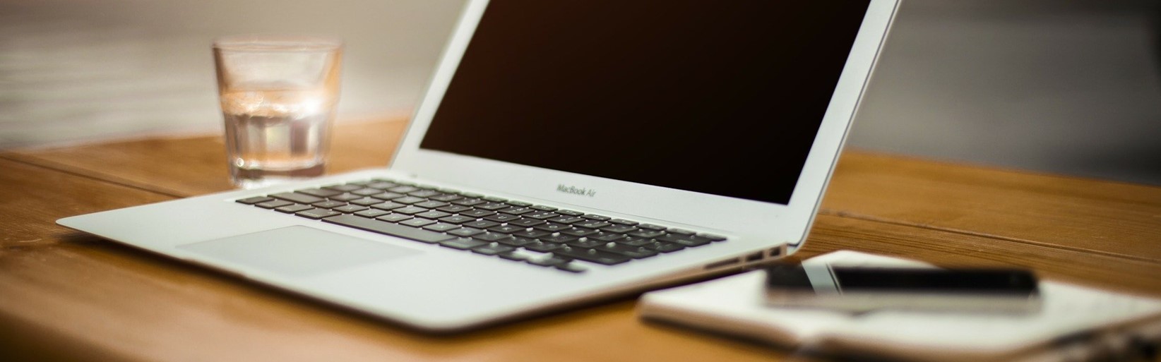 Aufgeklappter Laptop mit Handy und einem Glas Wasser