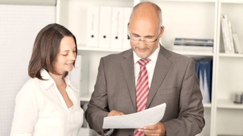 Zwei Personen in Businessklamotten schauen gemeinsam auf ein Dokument 