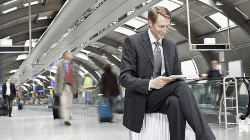 Mann im Anzug sitzt am Bahnhof auf seinem Koffer