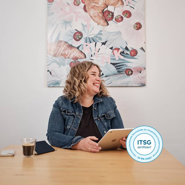 Lachende Frau sitzt vorm Schreibtisch am Laptop